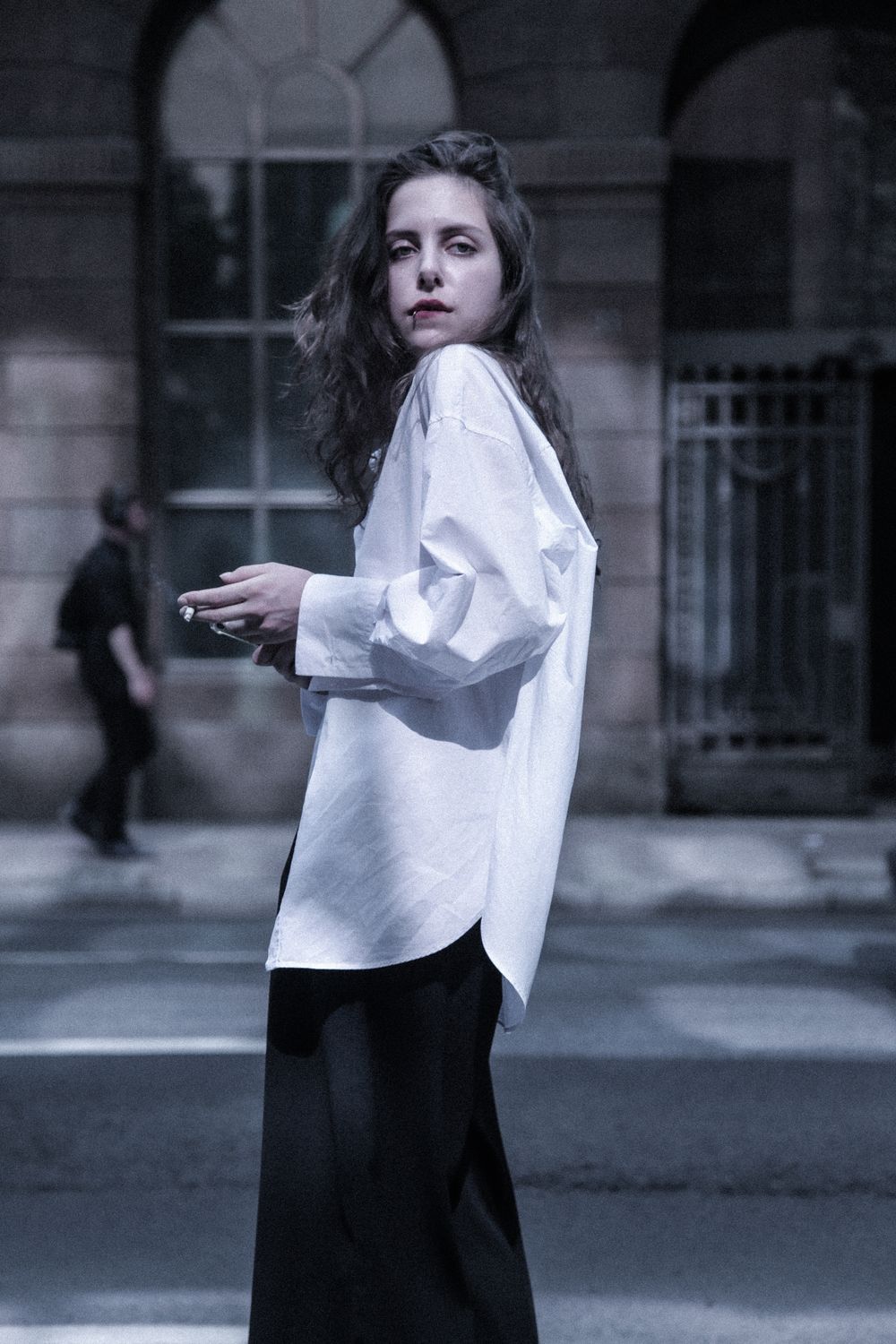 Loose white button-up shirt and black trousers worn outdoors against city architecture