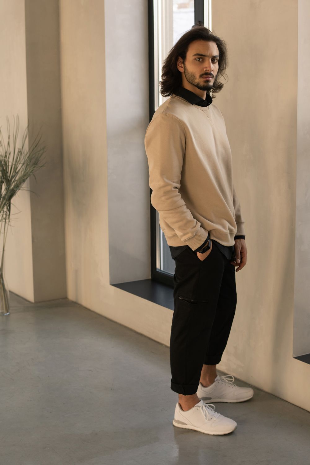 Beige sweater layered over a dark collared shirt with black trousers and white sneakers