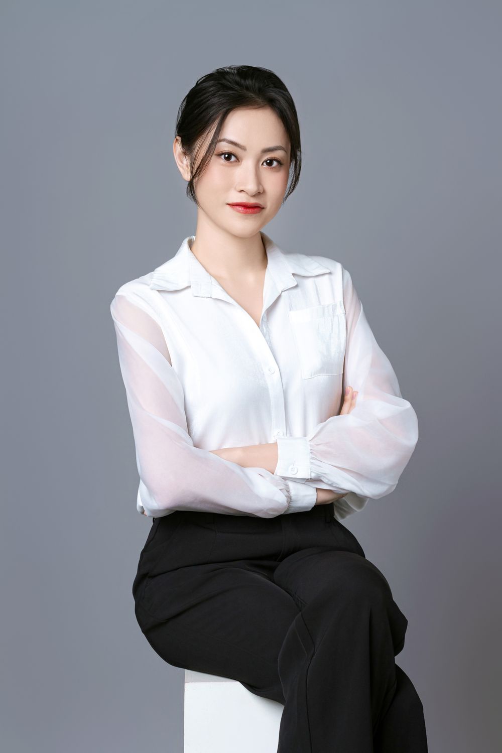 White collared blouse and black tailored trousers in a seated studio portrait