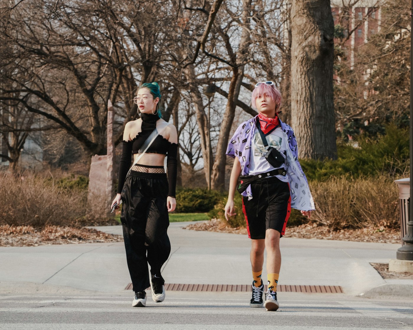 Two people mixing black silhouettes, a purple printed shirt, and colorful accessories on a city walk