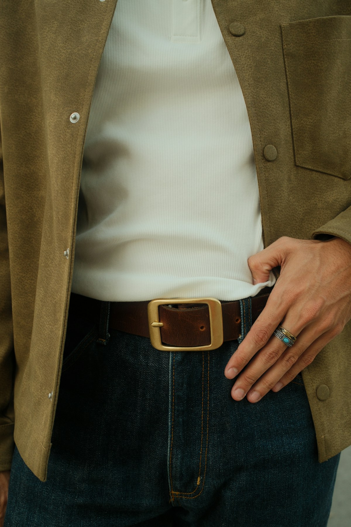 Close-up of a textured brown jacket, ribbed white top, leather belt, and dark denim