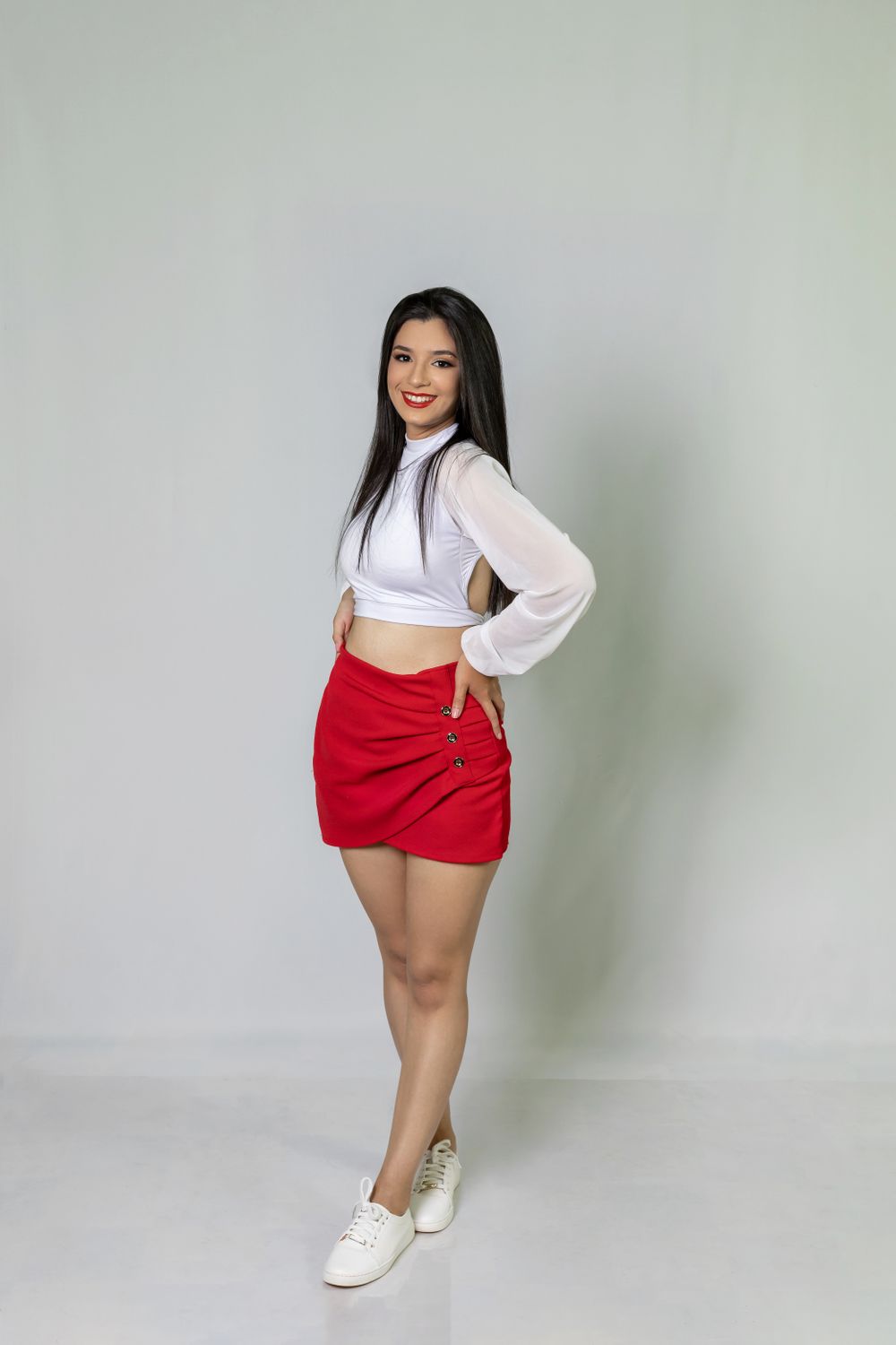 White long-sleeved crop top and red skirt styled with white sneakers against a neutral backdrop